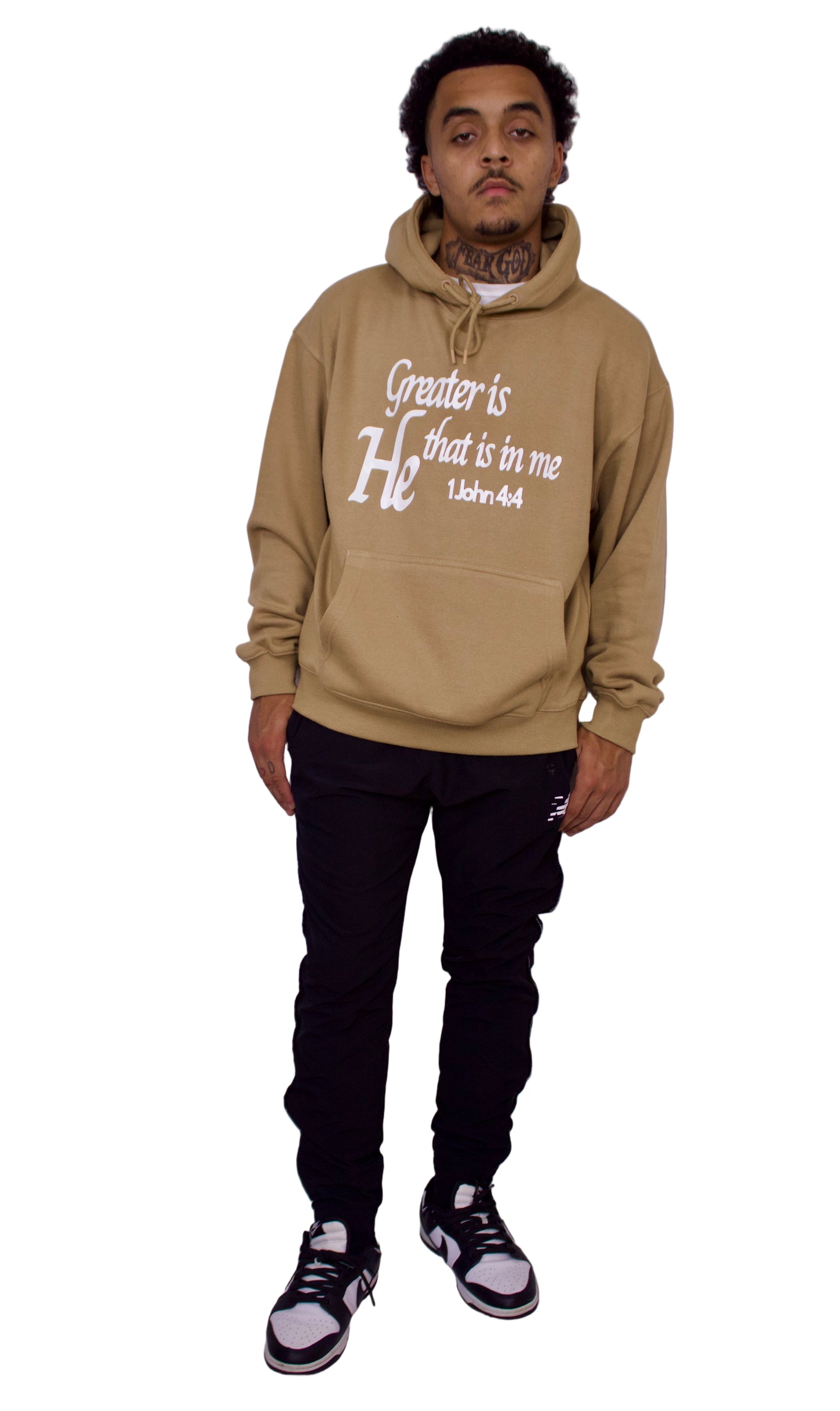 Person wearing a light brown hoodie with text, black pants, and black and white sneakers on a plain background